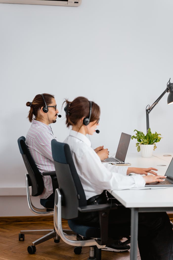 Two call center employees working with laptops and headsets in an office.